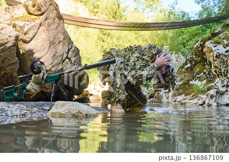 Camouflaged Sniper Washing Face in River During Field Training Near Rocky Creek and Footbridge 136867109