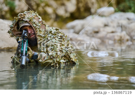 Camouflaged Sniper Soldier Lying in Shallow River With Rifle and Scope During Reconnaissance Camouflaged Sniper Soldier Lying in Shallow River With Rifle and Scope During Reconnaissance 136867119