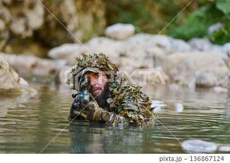 Camouflaged Sniper in Ghillie Suit Aiming Rifle While Partially Submerged in River Camouflaged Sniper in Ghillie Suit Aiming Rifle While Partially Submerged in River 136867124