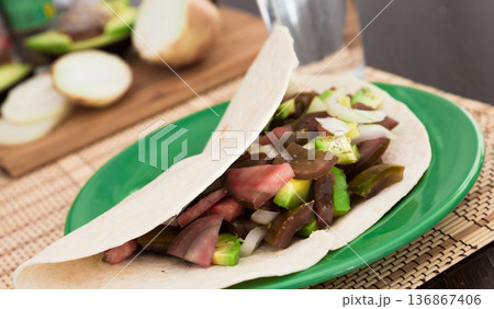 salad of black tomatoes, avocado and onions in Italian tortilla on green plate 136867406