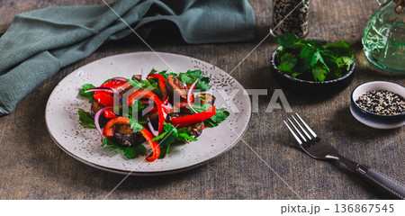 Warm salad with fried eggplant, bell pepper, onion, and herbs on a plate on the table web banner 136867545