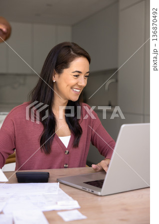 Smiling woman managing bills using laptop at home 136870492