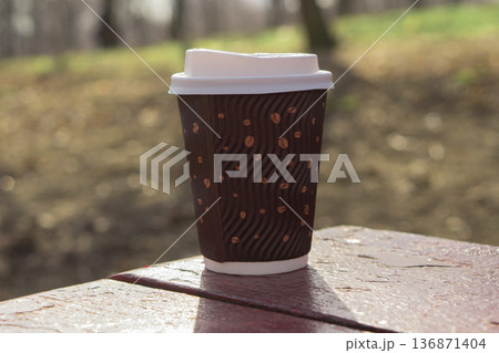 Disposable coffee cup with a lid stands on a blackboard in a park area Disposable coffee cup with a lid stands on a blackboard in a park area 136871404