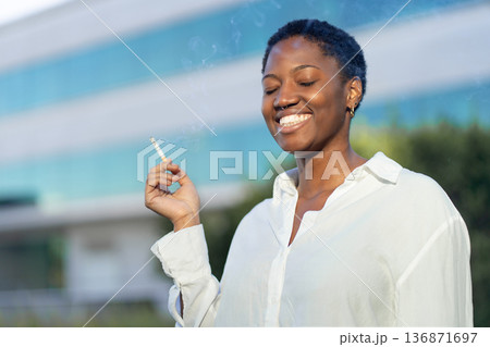 Smiling businesswoman smoking against modern 136871697