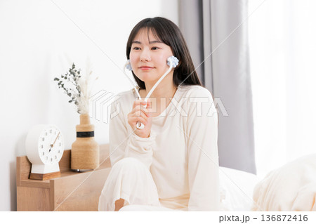 美顔器でマッサージするパジャマ姿の若いアジア人女性　 136872416