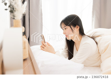 ベッドで寝ながらスマホを使う女性 ベッドで寝ながらスマホを使う女性 136872418
