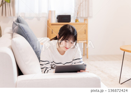 ソファに寝転がってタブレットPCを見る女性 ソファに寝転がってタブレットPCを見る女性 136872424
