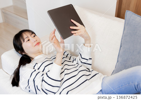 ソファに寝転がってタブレットPCを見る女性 136872425