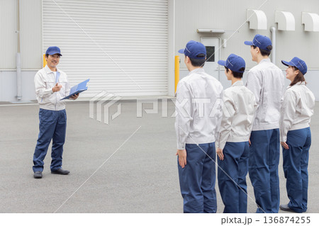 工場の前で朝礼をする作業員グループ 136874255