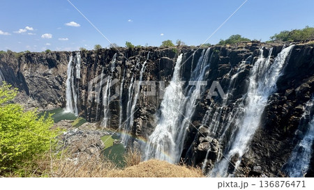 ザンビアのビクトリアフォールを対岸から撮影した晴天の昼の滝風景 観光旅行向け背景素材 136876471