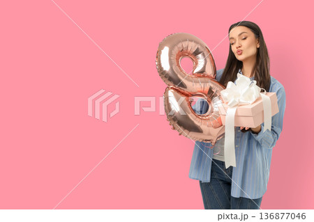 A young woman holds a present and a balloon showing the number 8 A young woman holds a present and a balloon showing the number 8 136877046