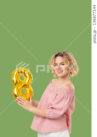 Woman holds a gold balloon number 8, smiling Woman holds a gold balloon number 8, smiling 136877144