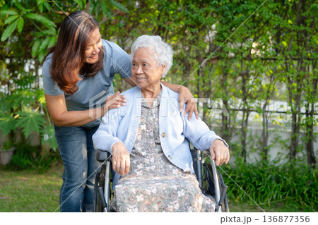 Caregiver help Asian elderly woman disability patient sitting on wheelchair in park. 136877356