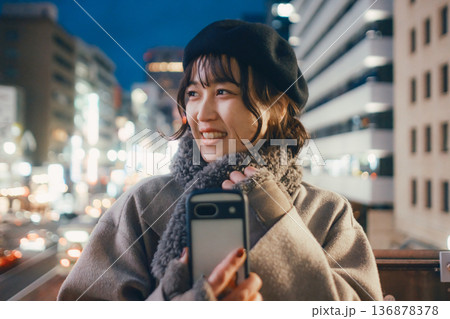 夜の都会でスマートフォンを使う笑顔の日本人女性 136878378