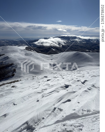 Snow-covered mountain ridge and winter landscape with clouds and distant peaks under blue sky 136878602