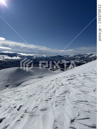Snow-covered mountain slope and wide winter landscape under clear blue sky with sunlight and distant peaks Snow-covered mountain slope and wide winter landscape under clear blue sky with sunlight and distant peaks 136878612