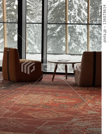 Cozy hotel lobby seating with low chairs and table overlooking snowy forest through floor-to-ceiling windows 136878614
