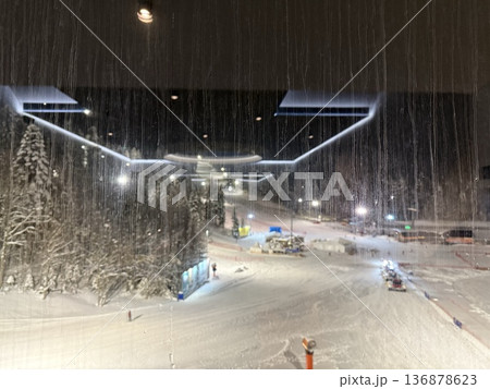 Nighttime ski resort slope seen through a wet window with reflections and snowy trees Nighttime ski resort slope seen through a wet window with reflections and snowy trees 136878623