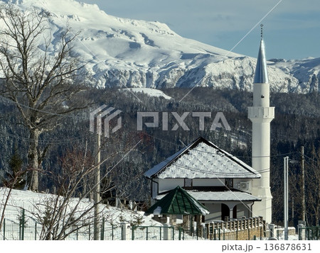 Snow-covered mosque with minaret in a mountain village landscape under winter skies 136878631