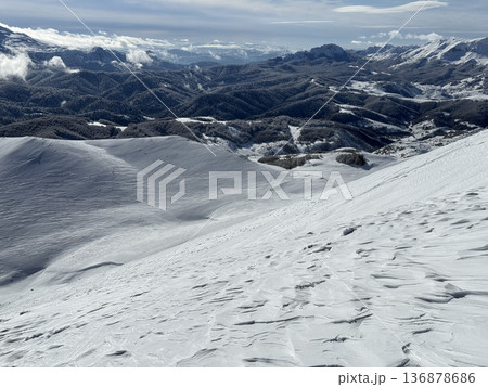 Snowy mountain landscape with rolling winter hills and distant forested ridges under blue sky 136878686