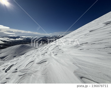 Sunlit snow slope and distant alpine peaks under clear blue winter sky Sunlit snow slope and distant alpine peaks under clear blue winter sky 136878711