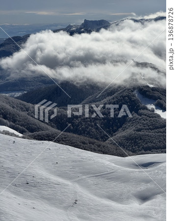 Snowy mountain landscape with low clouds rolling over forested ridges on a winter day 136878726