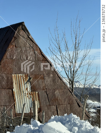 Rusty barn roof and snowdrift against a winter mountain landscape with bare trees 136878732
