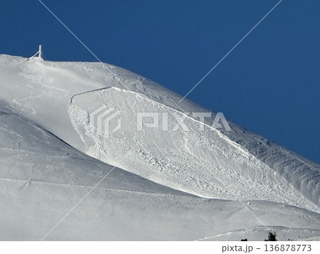 Snow-covered mountain peak with avalanche slab and cornice under a clear blue sky 136878773