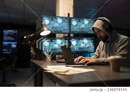 Adult male developer focusing intensely on encrypted network activity. Cybersecurity specialist types new software lines, detects threats and strengthens system defenses through diligent monitoring. 136879334