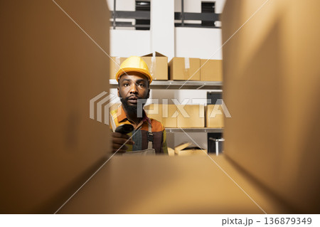 Black employee using a barcode scanner to update inventory system, managing products for e-business shipments, parcel express deliveries and retail order processing. Quality control. 136879349