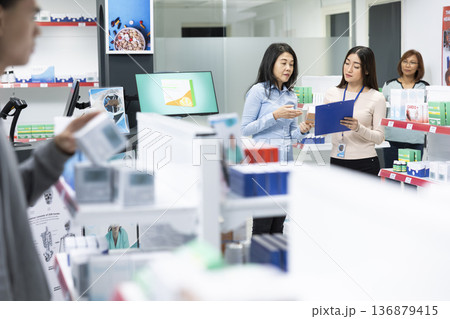Asian drugstore attendant explains prescription and health insurance details to female customer in modern pharmacy. Informative consultation emphasizes healthcare support and patient understanding. Asian drugstore attendant explains prescription and health insurance details to female customer in modern pharmacy. Informative consultation emphasizes healthcare support and patient understanding. 136879415