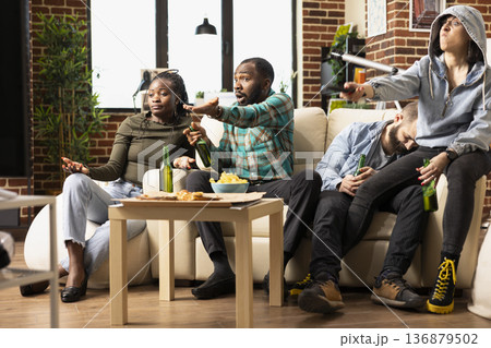 Multiethnic group in living room watching live football match, disappointed after team miss crucial goal. African American and Caucasian friends frown at TV, reacting with frustration after game loss. Multiethnic group in living room watching live football match, disappointed after team miss crucial goal. African American and Caucasian friends frown at TV, reacting with frustration after game loss. 136879502