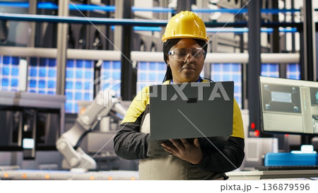 Engineer performing predictive maintenance using laptop, analyzing IoT sensor data, managing operational reliability of photovoltaic systems in smart factory environment, camera B 136879596
