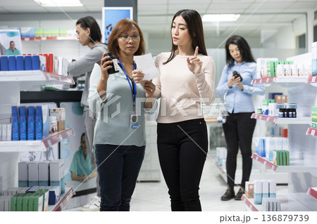 Female pharmacy employee discusses prescription details and health supplements with middle aged customer in modern drugstore. Focus on medical consultation, healthcare advice and patient support. Female pharmacy employee discusses prescription details and health supplements with middle aged customer in modern drugstore. Focus on medical consultation, healthcare advice and patient support. 136879739