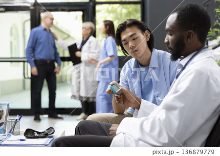 African american doctor measures blood sugar levels with precision during clinic visit. Asian man receives attentive care using medical equipment, supporting diagnosis, health monitoring and treatment 136879779