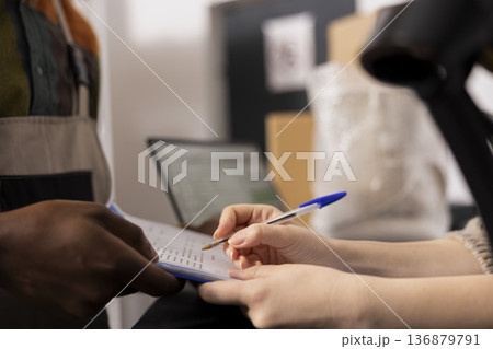 Close up of woman reviewing inventory list before packing goods for delivery, confirming the order processing operation sin house and managing the logistics side of the small business depot. 136879791