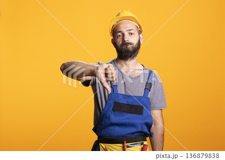 Male builder gestures thumbs down, expressing dissatisfaction or disapproval. Portrait of construction worker on yellow background representing evaluation, feedback or negative review at building site Male builder gestures thumbs down, expressing dissatisfaction or disapproval. Portrait of construction worker on yellow background representing evaluation, feedback or negative review at building site 136879838