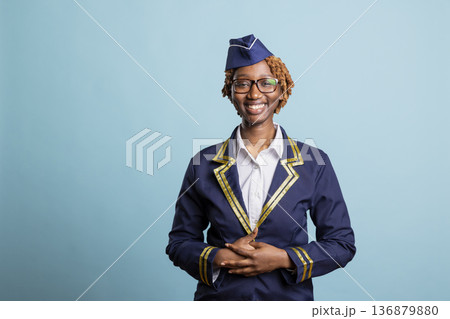 Friendly black woman in flight attendant uniform looking at camera with radiant smile against isolated background. African american air hostess posing for professional airline company portrait. Friendly black woman in flight attendant uniform looking at camera with radiant smile against isolated background. African american air hostess posing for professional airline company portrait. 136879880