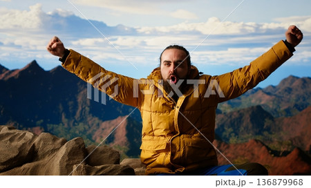 Determined climber standing at the summit enjoys peaceful moment of success. Vast sky, mountain range and fresh air highlighting the essence of freedom, wellness and exploration. Camera B. 136879968