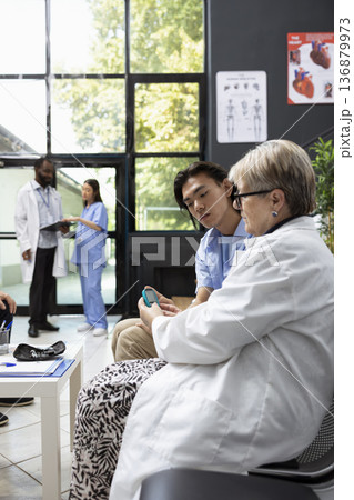 Medical professional checks patient blood glucose level with digital glucometer in clinic waiting area. The routine screening helps ensure proper health assessment before upcoming appointment. 136879973
