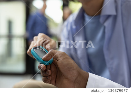 African american physician performs routine blood glucose test using test strip and digital glucometer. Patient sits calmly in clinic waiting area during standard healthcare appointment and diagnosis. African american physician performs routine blood glucose test using test strip and digital glucometer. Patient sits calmly in clinic waiting area during standard healthcare appointment and diagnosis. 136879977