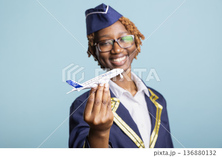 Playful flight attendant holds commercial scale plane, standing in studio with blue background. Joyful woman represents aviation dreams, global travel and passion for airline service and tourism. Playful flight attendant holds commercial scale plane, standing in studio with blue background. Joyful woman represents aviation dreams, global travel and passion for airline service and tourism. 136880132