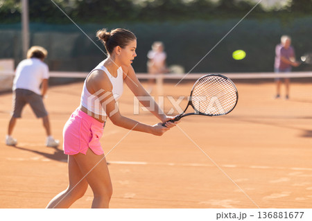 Padel tennis couple in court playing double match. Young beautiful woman in white t-shirt hits tennis ball with racket 136881677
