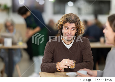Happy middle-age man and young girl chatting over cup of coffee at table in light cafe, face of middle-age man and back of girl Happy middle-age man and young girl chatting over cup of coffee at table in light cafe, face of middle-age man and back of girl 136881690