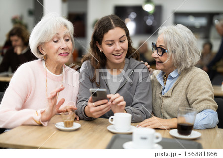 Young woman showing photos on phone elderly to women Young woman showing photos on phone elderly to women 136881866