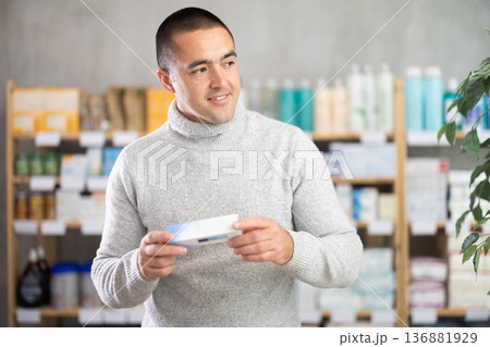 Young man chooses ointment at pharmacy Young man chooses ointment at pharmacy 136881929