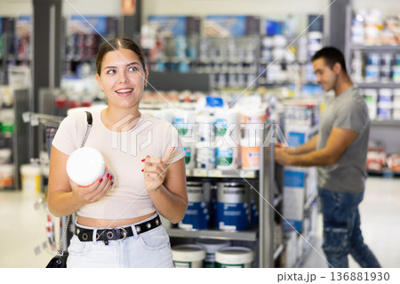 Woman chooses and buys can of paint at hardware shop Woman chooses and buys can of paint at hardware shop 136881930