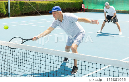 Man with black racket playing match in open behind net court outdoors. Man with black racket playing match in open behind net court outdoors. 136881966