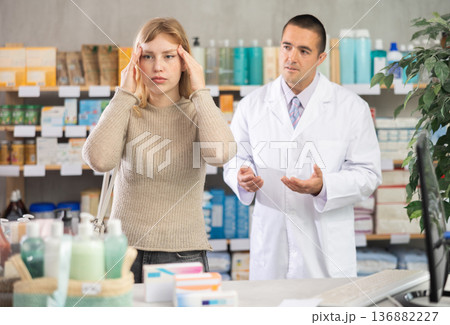 Young woman having headache while pharmacist offering in drugstore Young woman having headache while pharmacist offering in drugstore 136882227