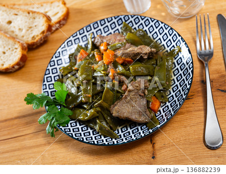 There is plate with braised french green bean and carrot and beef tenderloin stew on wooden table. 136882239